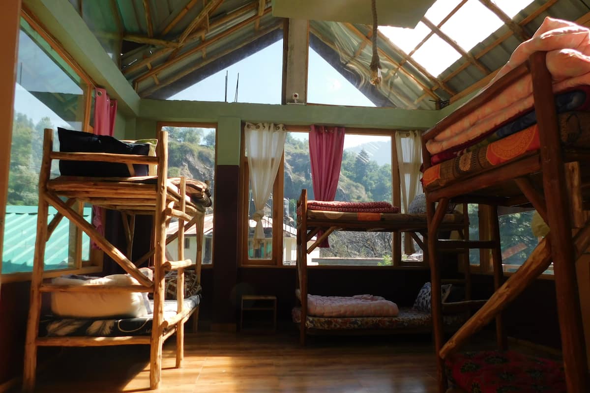 Une chambre rustique avec des lits superposés en bois, une échelle en bois et une petite table. De grandes fenêtres laissent entrer la lumière naturelle et offrent une vue sur le paysage environnant.