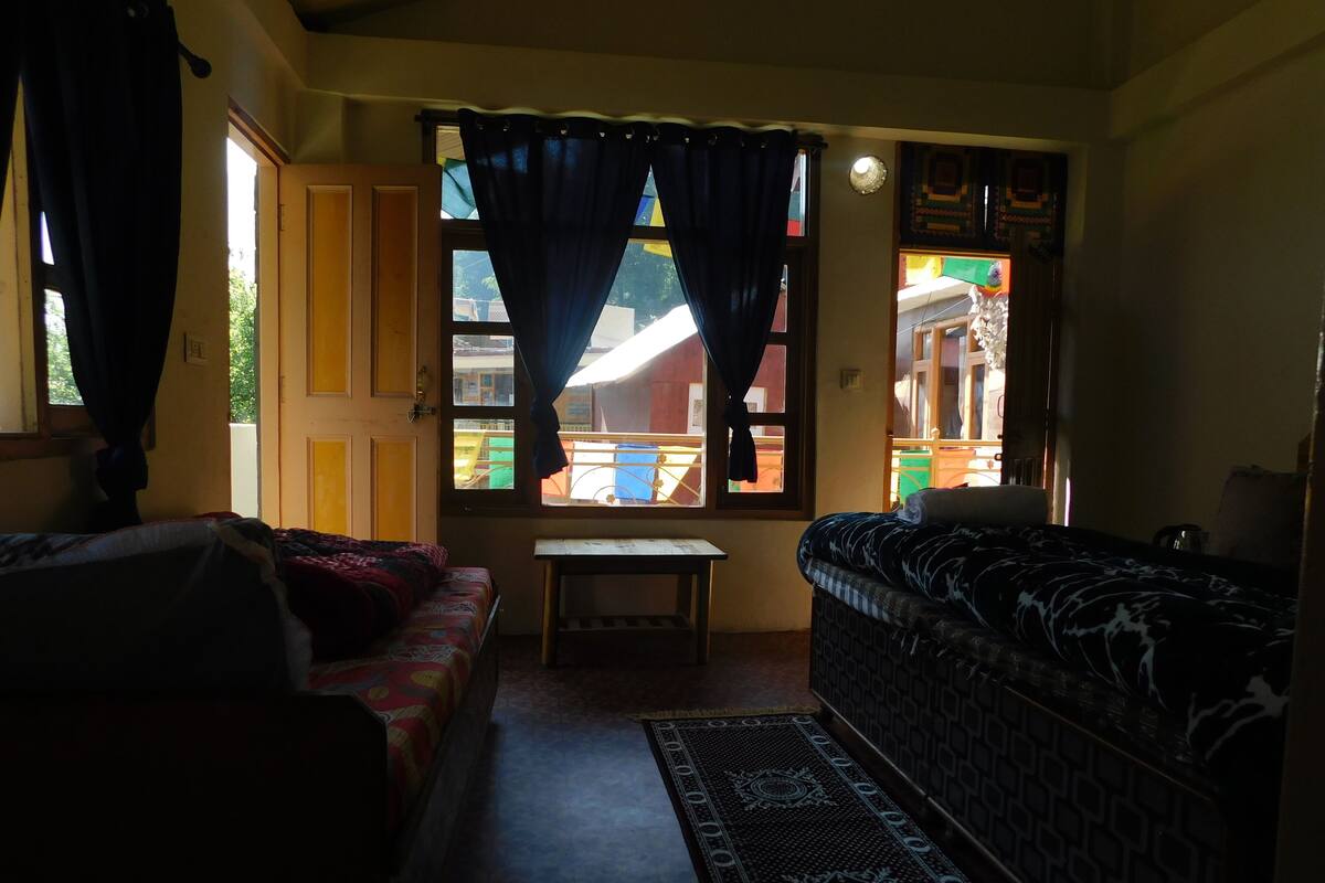 Une chambre avec deux lits, une petite table et une fenêtre avec des rideaux.