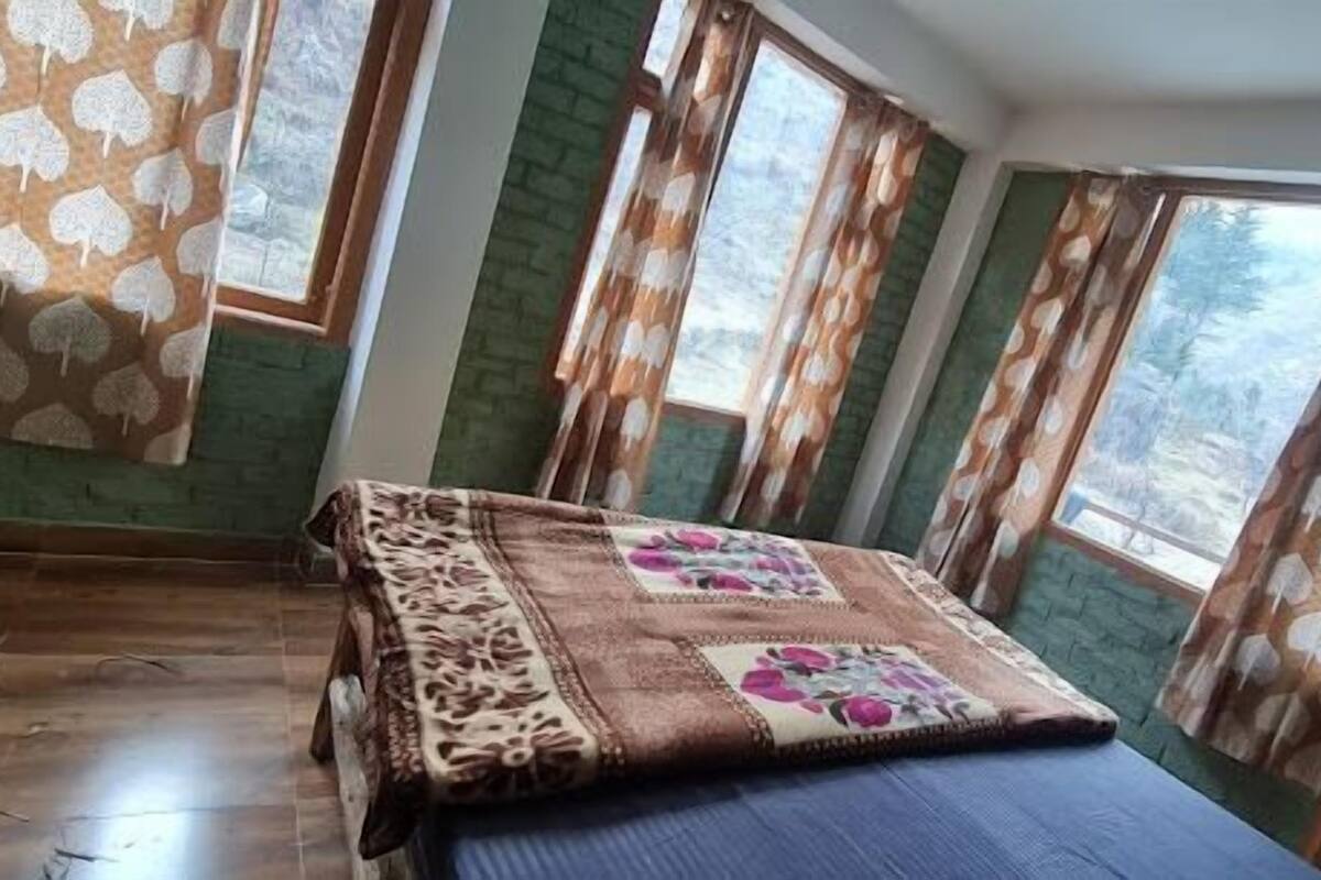 Une chambre avec un lit, un plancher en bois et de grandes fenêtres ornées de rideaux à motifs.
