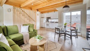 Un salon moderne avec un canapé vert, un plafond en bois et un coin repas comprenant une table ronde et des chaises.
