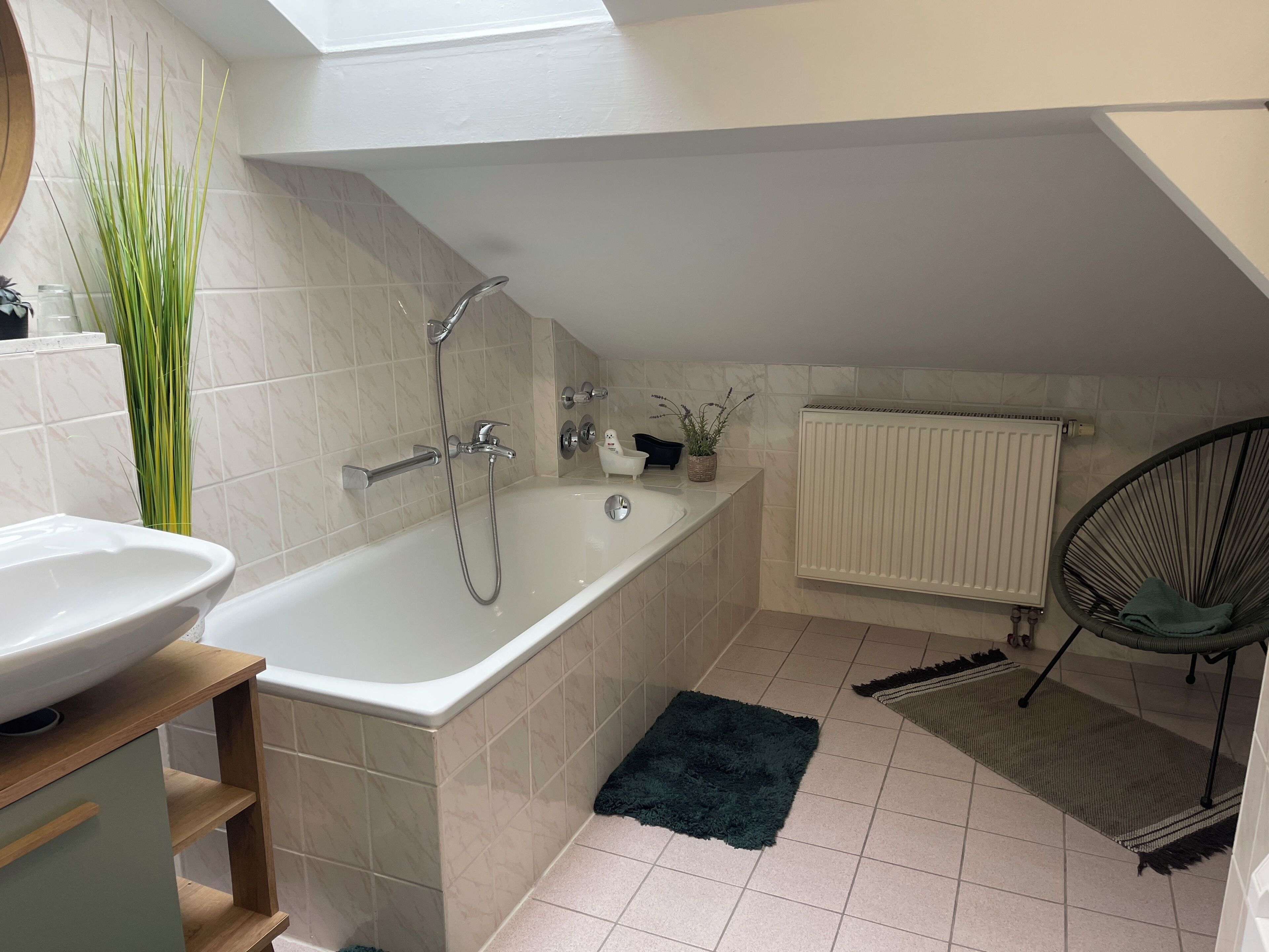 Une salle de bain moderne avec une baignoire, un lavabo, un radiateur, une chaise et une plante en pot.