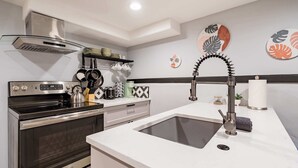 Une cuisine moderne dotée d’une cuisinière en acier inoxydable, d’un four encastré, d’un plan de travail blanc et d’un évier avec un robinet au design contemporain.