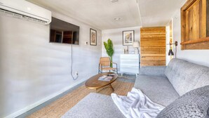 Un salon moderne avec un canapé, une table basse et un téléviseur. On y trouve également une plante et un panneau mural en bois.