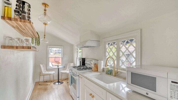 A modern kitchen with white cabinetry, a gas stove, a microwave, and a window with a lattice design.