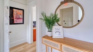 A hallway with a framed abstract painting, a potted plant, a framed map of Portland, and a mirror on a wooden console.