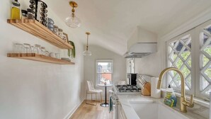 A modern kitchen with wooden shelves, a white countertop, a sink with a gold faucet, and a window with a view.