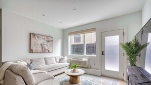Ein Wohnzimmer mit Sofa, Couchtisch und einem großen Fenster mit Jalousien.