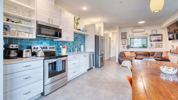 A modern kitchen with white cabinetry, a stainless steel refrigerator, and a dining area with a wooden table and chairs. - Luxury Penthouse - Rooftop Deck - 3BR - AC (Portland)