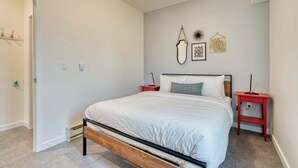 A bedroom with a bed, two nightstands, a heater, and wall decorations. - Luxury Penthouse - Rooftop Deck - 3BR - AC (Portland)