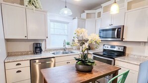 A modern kitchen with white cabinets, stainless steel appliances, a wooden dining table, and a green chair.