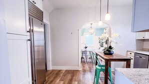 A modern kitchen with white cabinets, a stainless steel refrigerator, a wooden dining table, and a green chair.