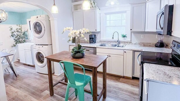 A compact kitchen with white cabinets, a wooden table, a teal chair, and a washing machine.