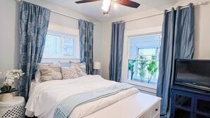 A bedroom with a bed, a dresser, a ceiling fan, and a TV.