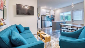 A modern living room with a teal sofa, a flat-screen TV, and a kitchen area with stainless steel appliances.