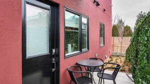 A modern building exterior with a black door, two windows, and a small patio area with a round table and chairs.