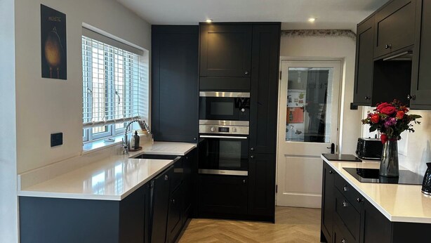 A modern kitchen with black cabinets, stainless steel appliances, and a wooden herringbone floor. - 3 Bed-sleeps 5-garden-parking-pets (Carlisle)