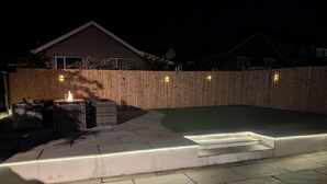 A backyard with a wooden fence, a small outdoor seating area with wicker furniture, and a paved patio. - 3 Bed-sleeps 5-garden-parking-pets (Carlisle)
