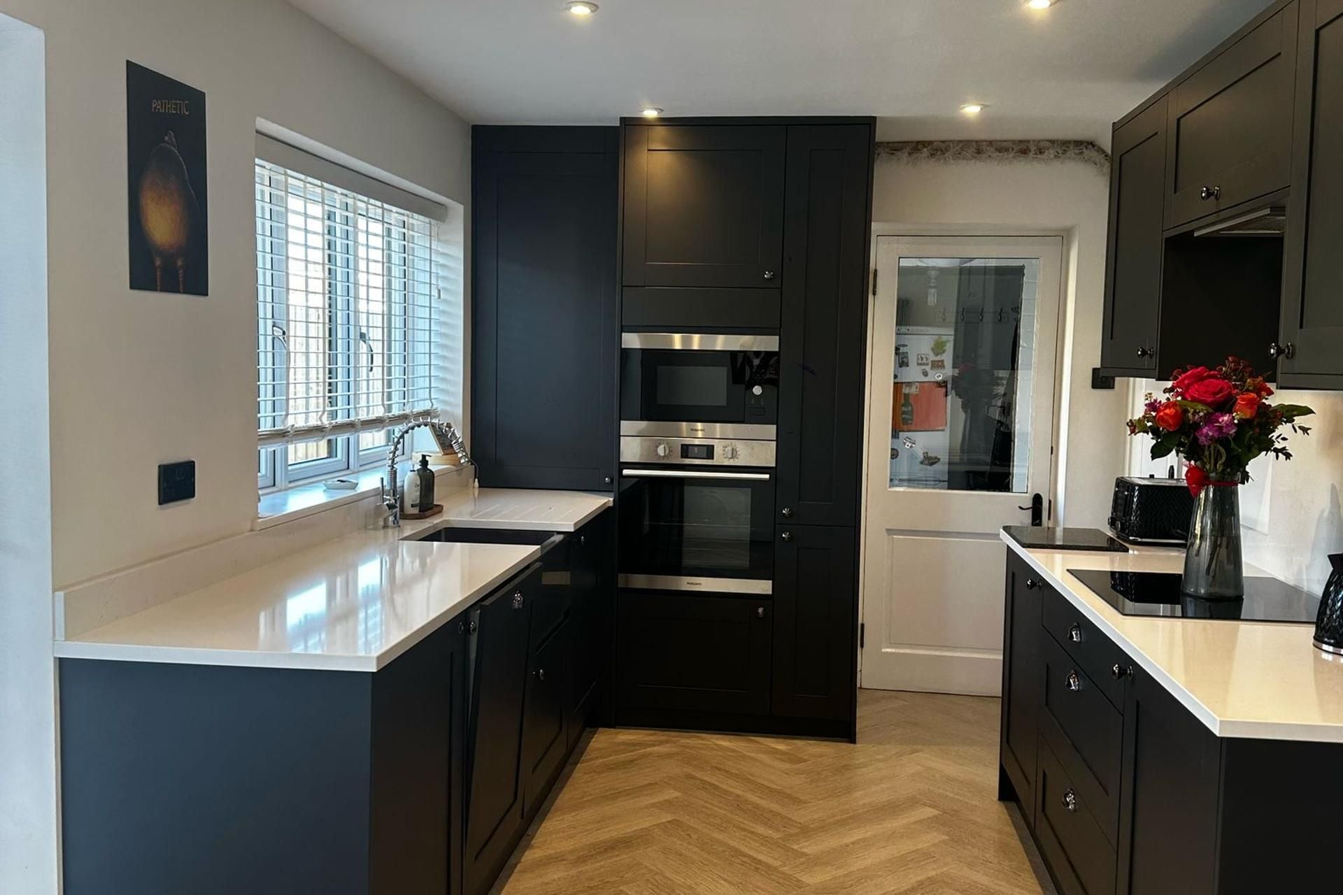 A modern kitchen with dark cabinetry, stainless steel appliances, and a herringbone wood floor.