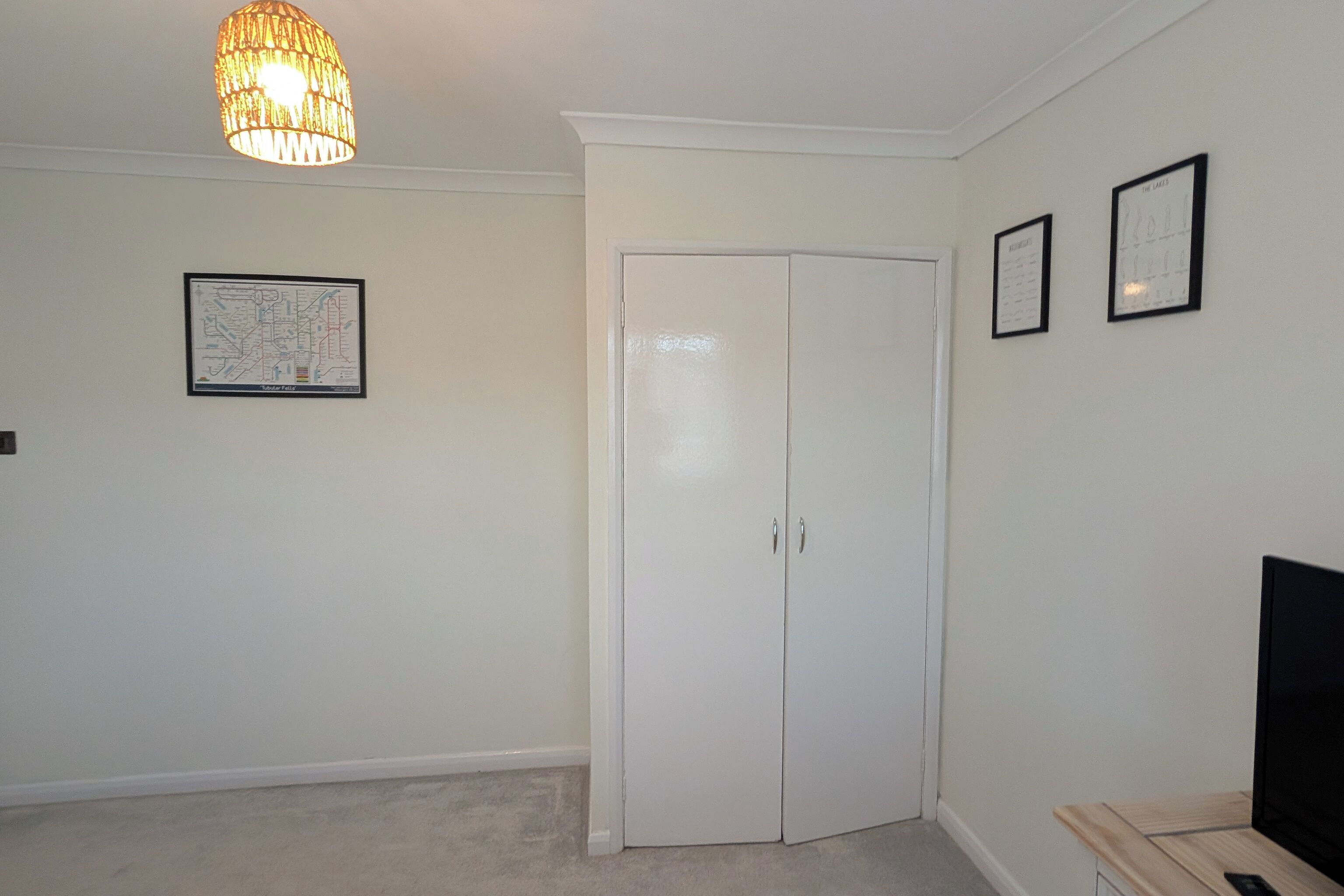 A room with a white door, a map on the wall, and a television on a wooden stand.