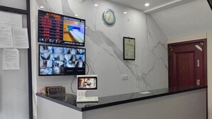Un'area reception di un hotel con una parete in marmo, un pannello segnaposti digitale, diverse telecamere di sicurezza, una sveglia e un certificato incorniciato.