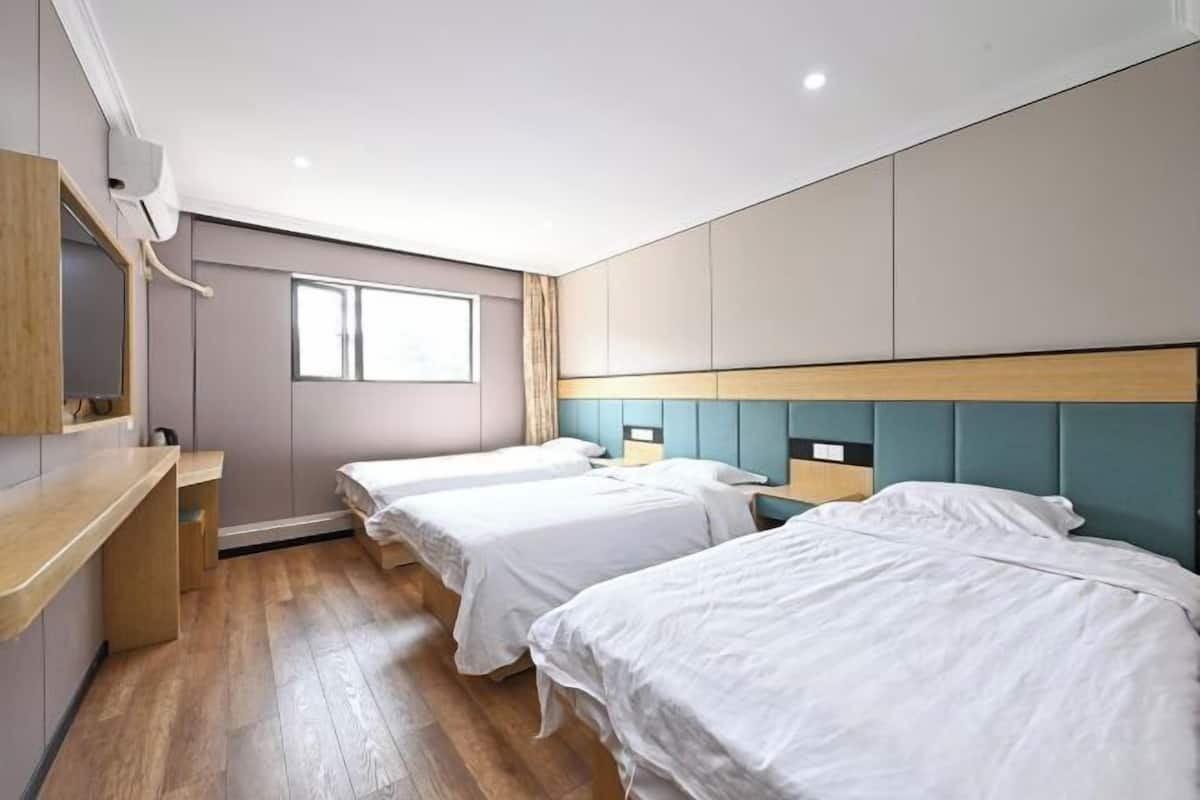 A hotel room with two beds, a wooden desk, a window, and a built-in wardrobe.