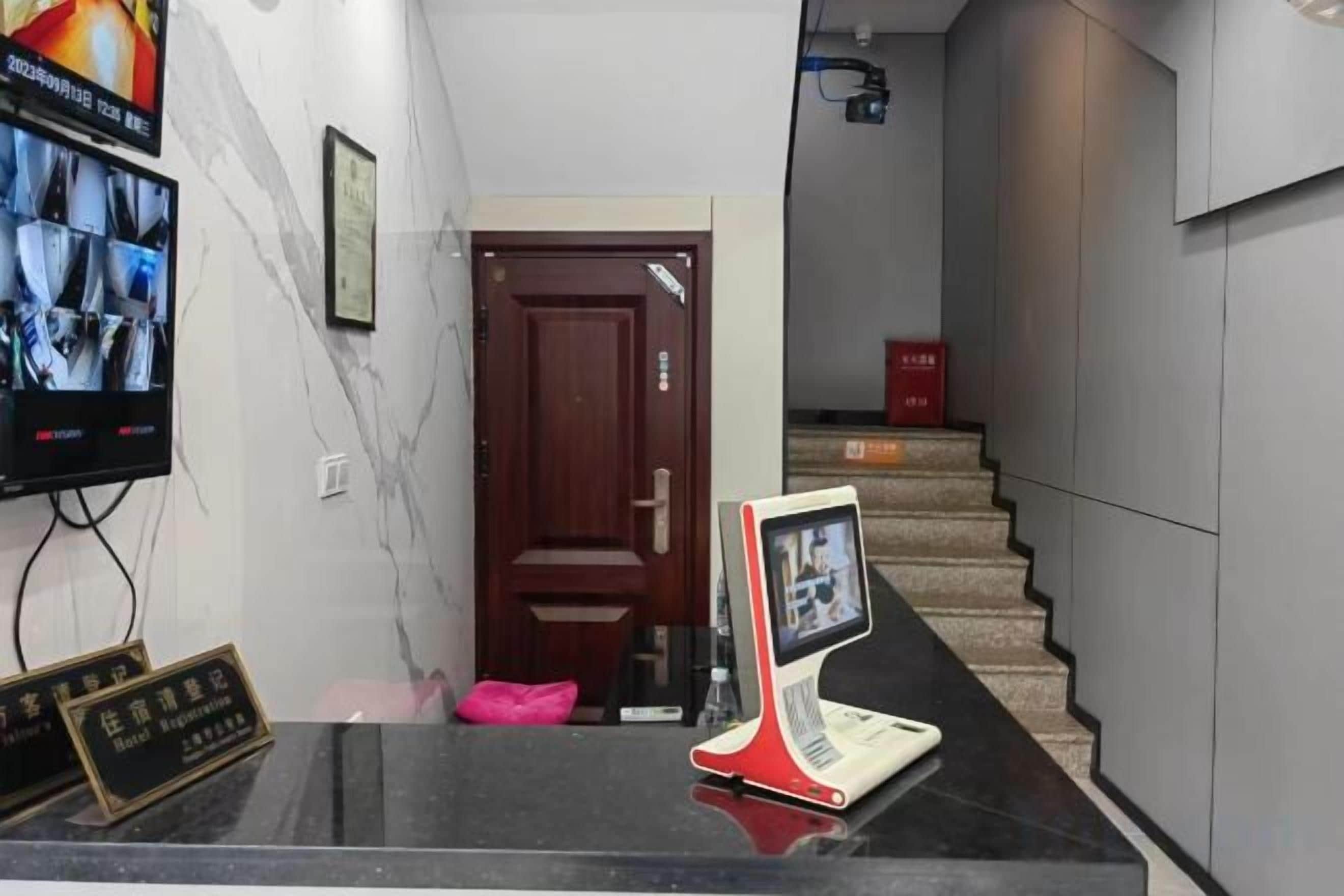 Un área de recepción con mostrador, televisor montado en la pared y una escalera que sube a un piso superior.
