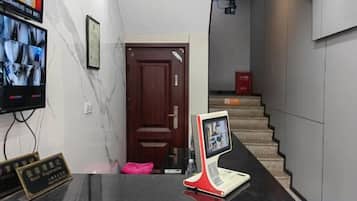Un área de recepción con mostrador, televisor montado en la pared y una escalera que sube a un piso superior.