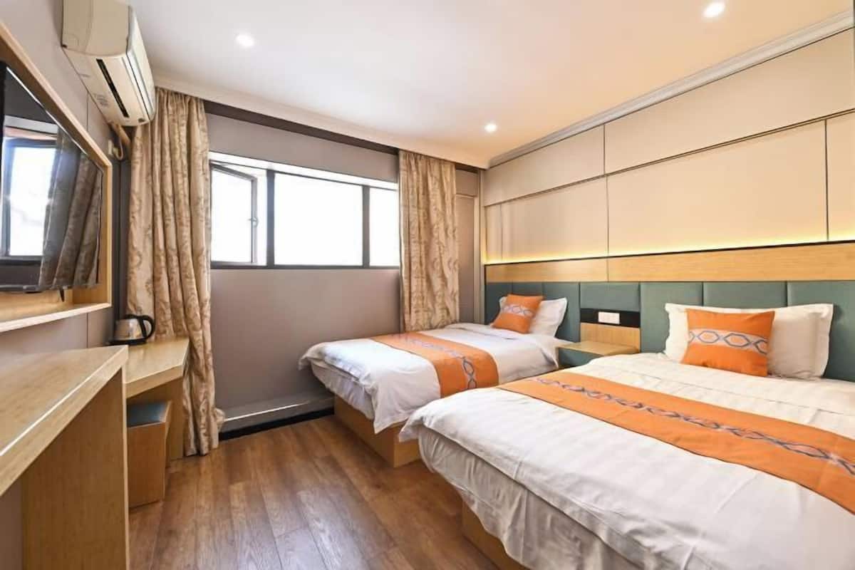 A hotel room with two beds, a desk, a TV, and a window with curtains.