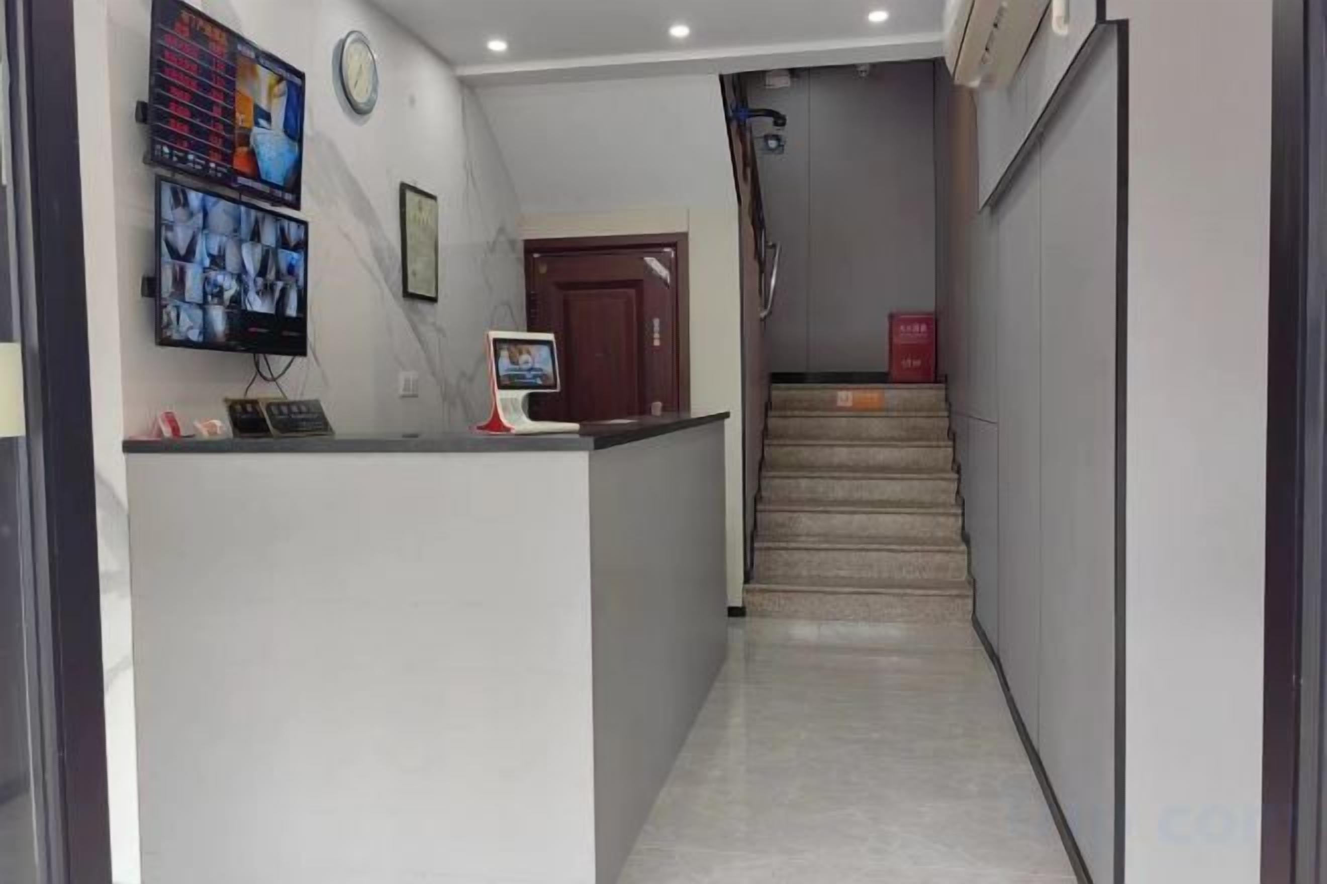 Un área de recepción con mostrador, un reloj y una escalera que sube a un piso superior.