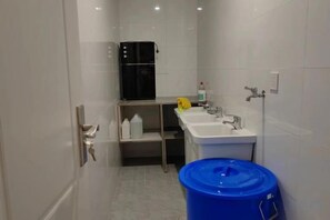 A small, modern bathroom with a black refrigerator, a sink, and a blue trash bin.
