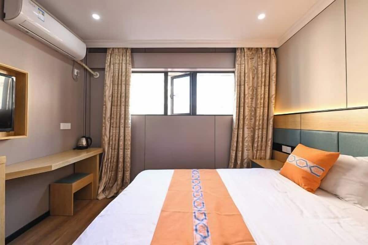 A hotel room with a bed, a desk, a chair, a window, and curtains.
