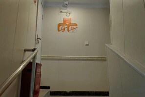 A narrow stairway with a handrail, a fire alarm, and a wall-mounted sign.