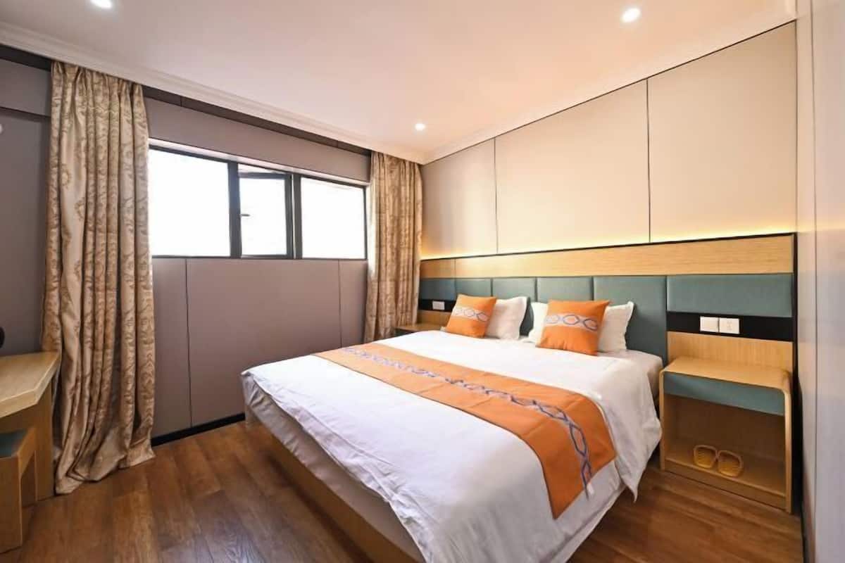 A hotel room with a large bed, a desk, a wardrobe, and a window with curtains.