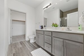 A modern bathroom with a walk-in shower, a toilet, and a vanity with a large mirror.