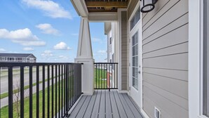 Ein überdachter Balkon mit Holzfußboden, weißen Wänden und einem schwarzen Geländer.