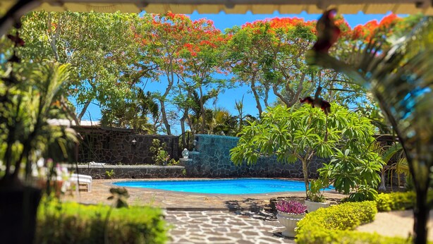 A pool area with a stone pathway, surrounded by lush greenery and flowering plants. - Charming villa in Pereybère and walking distance to the beach with private pool. (Grand Baie)