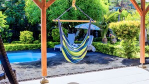 A hammock suspended between wooden beams in a lush garden with a pool. - Charming villa in Pereybère and walking distance to the beach with private pool. (Grand Baie)