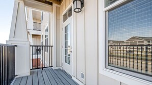 A balcony with a wooden deck, a white exterior wall, and a large window overlooking a building. - Stylish Stay | Near Everything! (Whitestown)