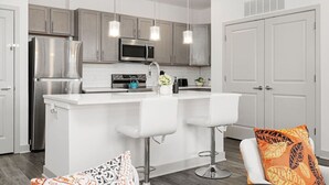 A modern kitchen with stainless steel appliances, a central island with bar stools, and a white color scheme. - Stylish Stay | Near Everything! (Whitestown)