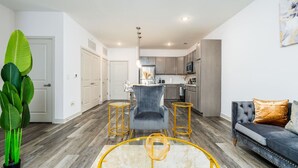 A modern living room with a grey sofa, a coffee table, and a dining area with a grey chair. - Refined Comforts: Luxe Stay in Whitestown Indiana (Perry Township)