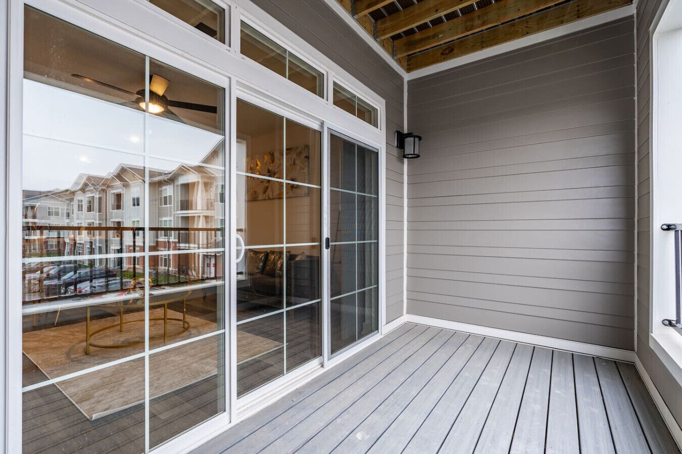 A covered patio with a wooden deck, large sliding glass doors leading to an interior space with a dining table and chairs, and a view of neighboring houses.