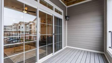 A covered patio with a wooden deck, large sliding glass doors leading to an interior space with a dining table and chairs, and a view of neighboring houses.