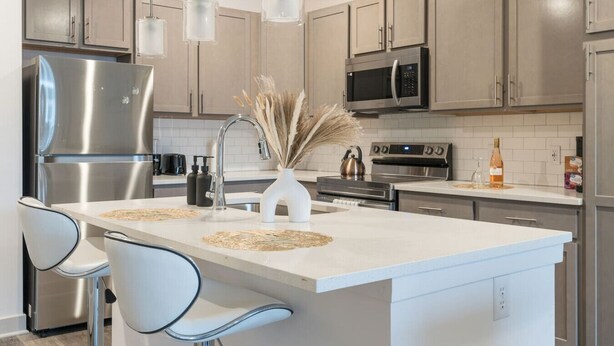A modern kitchen with stainless steel appliances, a central island with chairs, pendant lights, and a decorative vase. - Refined Comforts: Luxe Stay in Whitestown Indiana (Perry Township)