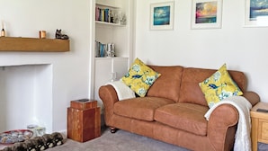 A cozy living room with a brown sofa, two yellow floral pillows, a bookshelf, and a mounted deer head. - Seasgair is a cosy property located in Dingwall, close to all local amenities. (Dingwall)