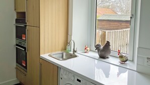 A kitchen with wooden cabinets, a stainless steel sink, and a window with a view of a backyard. - Seasgair is a cosy property located in Dingwall, close to all local amenities. (Dingwall)