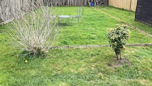 A backyard with a wooden fence, a small bush, and a metal chair. - Seasgair is a cosy property located in Dingwall, close to all local amenities. (Dingwall)
