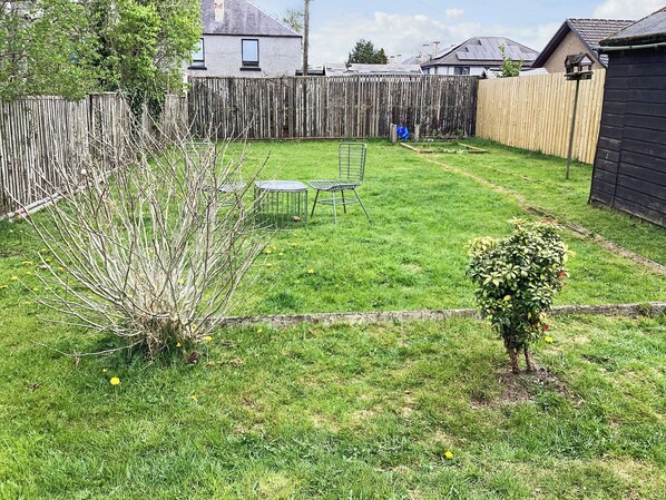 A backyard with a wooden fence, a small bush, and a metal chair. - Seasgair is a cosy property located in Dingwall, close to all local amenities. (Dingwall)