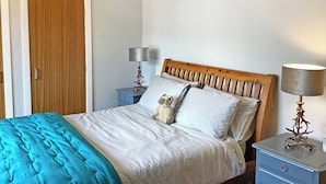 A bedroom with a wooden bed, a blue nightstand, a lamp, and a door. - Seasgair is a cosy property located in Dingwall, close to all local amenities. (Dingwall)