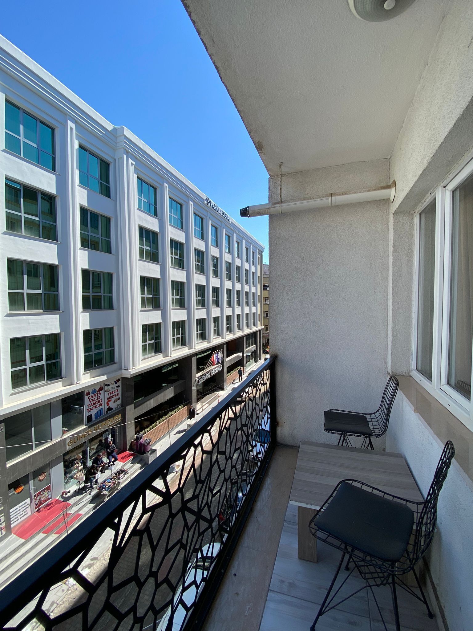 Varanda com mesa e cadeiras, dando vista para um edifício com várias janelas e uma placa.