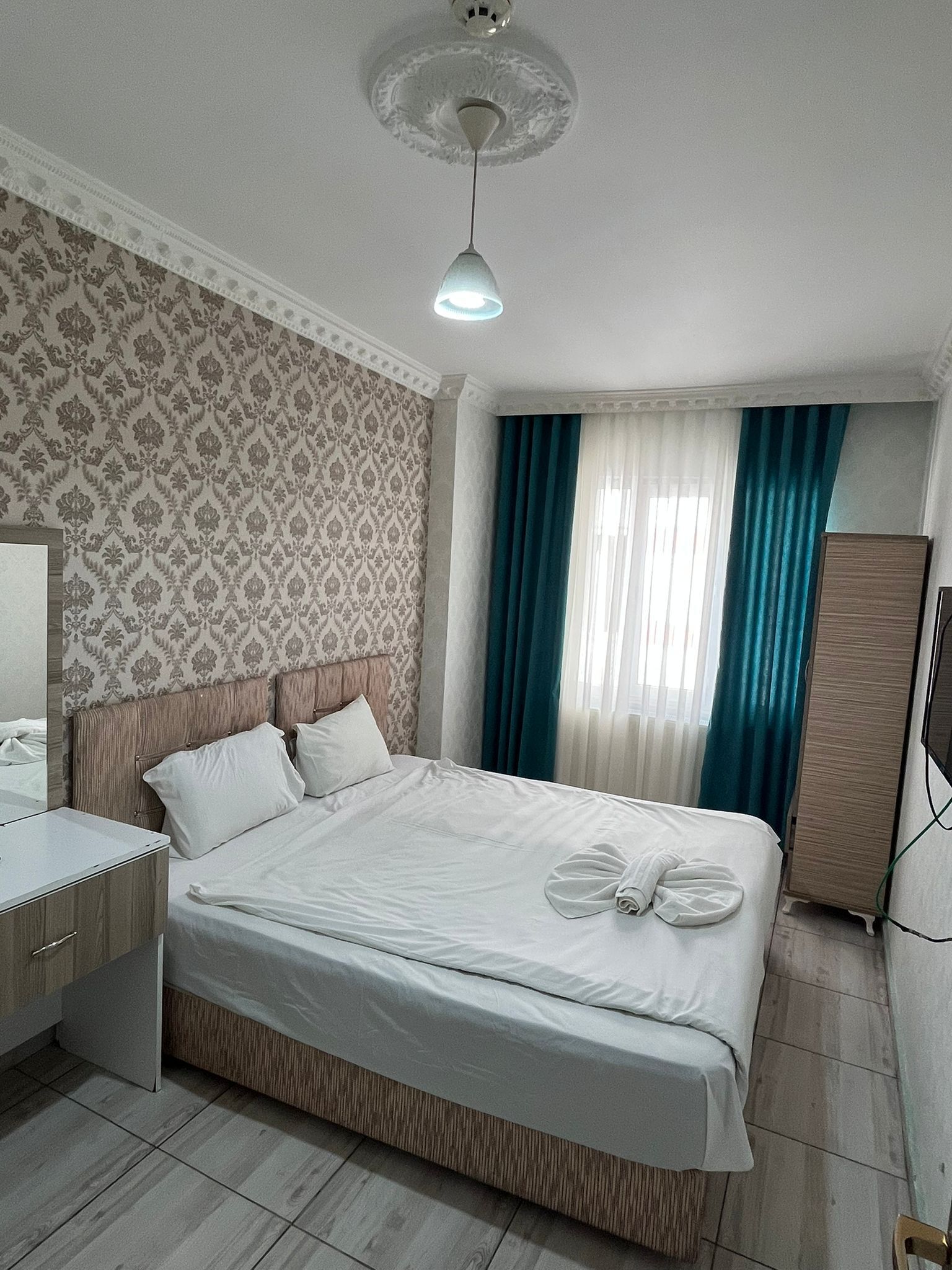 A hotel room with a bed, a bedside table, a wardrobe, and a ceiling light.